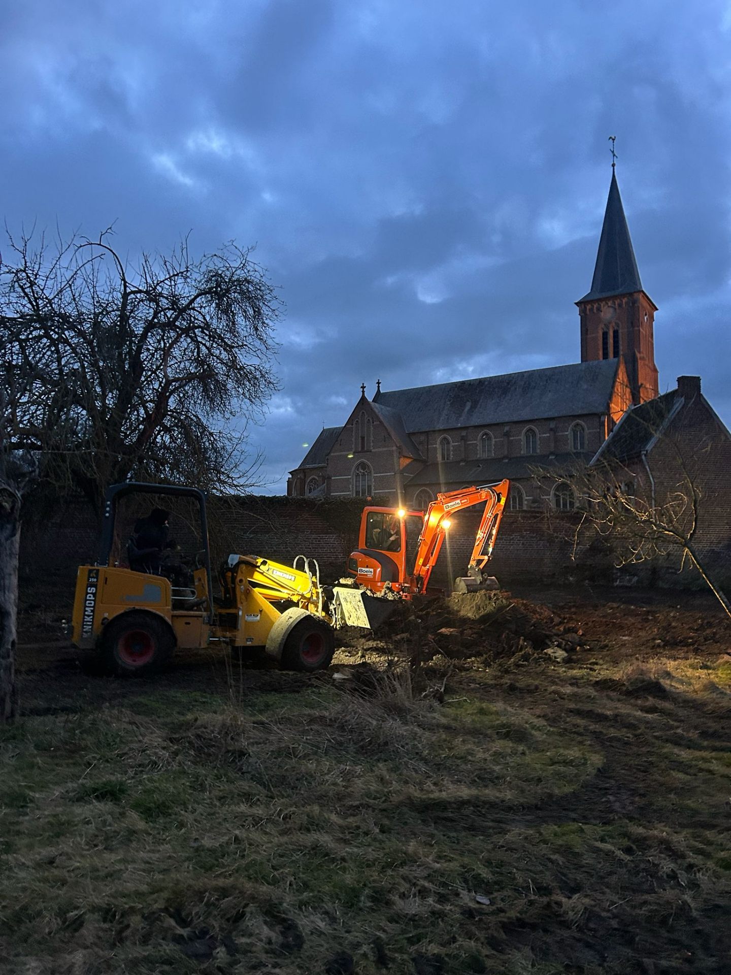 Knikmops 250 en minigraver aan het werk tijdens grondwerken bij een andere historische site in de schemering
