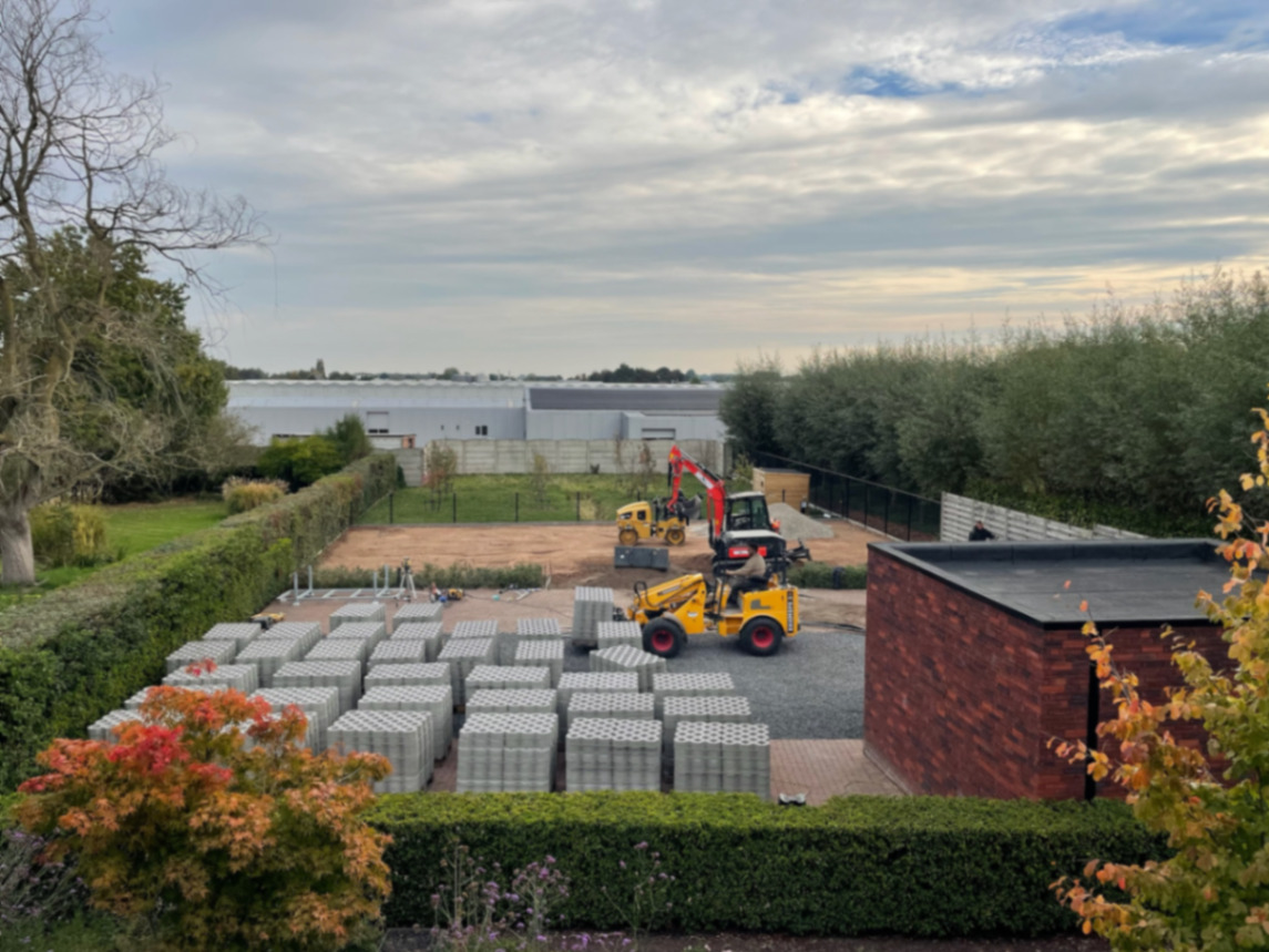 Aanleg van de bedrijfsparking met paletten waterdoorlatende klinkers en machines op de werf